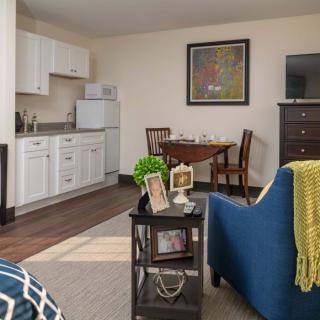 A cozy living area featuring a small kitchen, dining table, sofa with a throw blanket, and decorative accents.