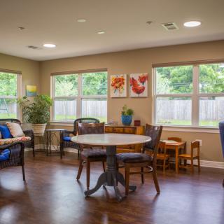 A cozy living room with large windows, featuring a round table and chairs on a wooden floor.