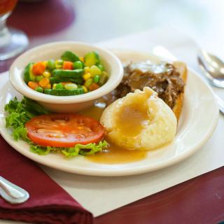 A plate featuring mashed potatoes with gravy, beef, a side of mixed vegetables, and sliced tomato.