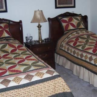 A cozy bedroom with twin beds featuring quilted bedding and a shared nightstand with a lamp.
