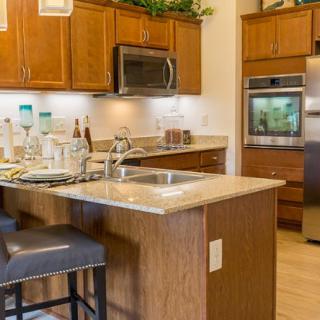 A modern kitchen with wooden cabinets, an island, stools, and stainless steel appliances.