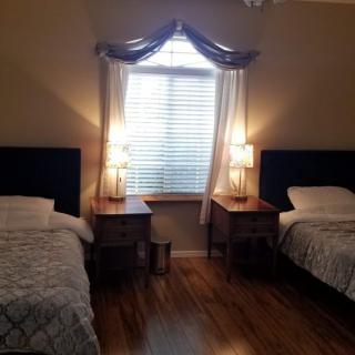 A cozy bedroom with two twin beds, nightstands, and lamps, featuring a window with curtains.