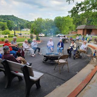 A group of people sitting around a fire pit outdoors with a scenic backdrop.