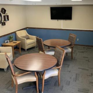 A cozy meeting room with round tables, chairs, and a television on the wall.
