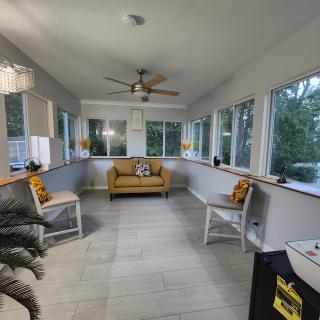 A cozy sunroom with ample windows, featuring a central sofa and chairs, adorned with cushions and a ceiling fan overhead.