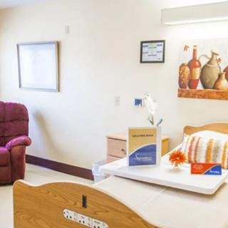 A well-lit hospital room with a bed, reclining chair, and decorative artwork on the wall.