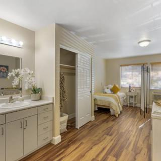 A well-decorated bedroom with wooden flooring, featuring a bed, a vanity area with a mirror, and neutral color tones.