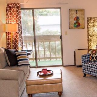 A cozy living room with a sofa, armchair, coffee table, and a sliding glass door leading to a balcony.