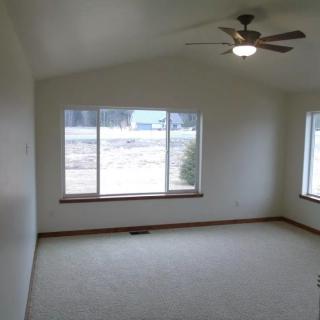 An empty room with large windows, a ceiling fan, and carpeted flooring.