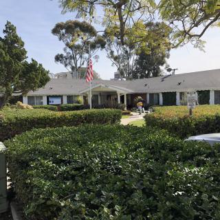 A school building surrounded by hedges and trees under a clear sky, with an American flag on a flagpole.