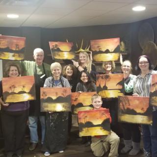 A group of people proudly displaying their completed paintings in an art class setting.