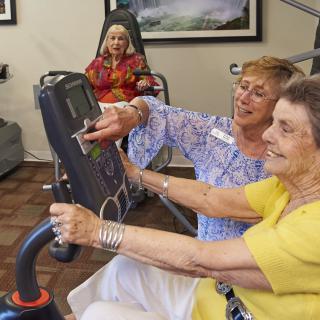 An elderly woman receives assistance while using exercise equipment in a community center.