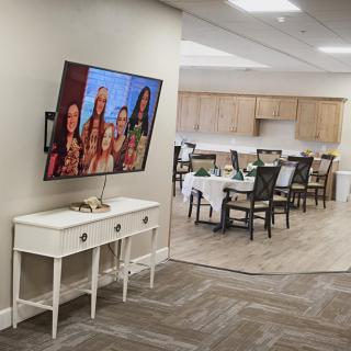 A modern living space featuring a wall-mounted television and a dining area in the background.