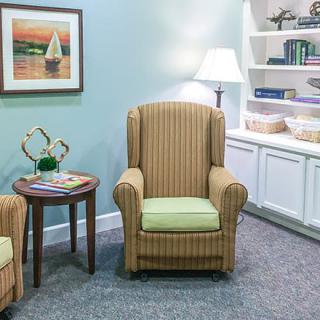 A cozy living room with a striped armchair, side table, and a warmly lit lamp beside a bookshelf.