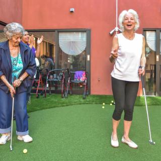 Two seniors enjoying a game of mini-golf outside.