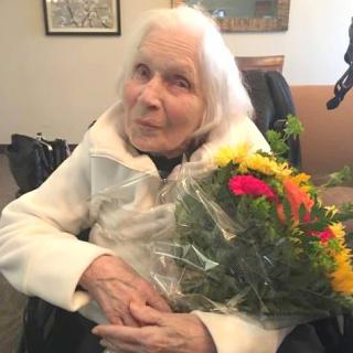 An elderly woman sitting in a wheelchair holding a bouquet of colorful flowers.
