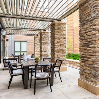 A modern outdoor patio with a pergola and stone columns, featuring a seating area with tables and chairs.