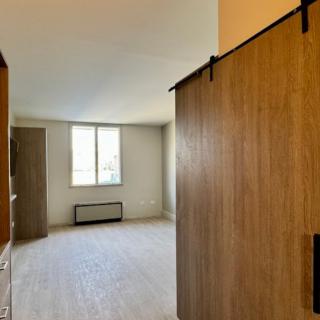 A spacious room with natural light coming through a window, featuring wooden sliding doors.