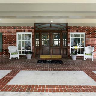 A welcoming entrance with glass doors and brick walls, flanked by white chairs and potted plants.