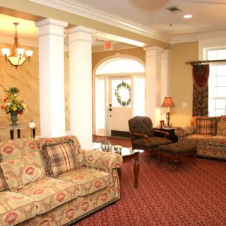 A cozy living room with elegant furniture and classic decor, featuring sofas, armchairs, and a chandelier.
