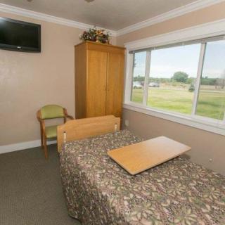 A simple bedroom with a bed, bedside table, chair, and television.