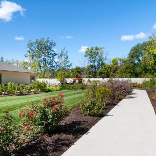 A scenic garden with a paved pathway, vibrant flowers, and lush greenery on a sunny day.