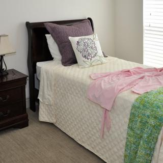 A neatly made single bed in a cozy bedroom with decorative pillows and a nightstand beside it.
