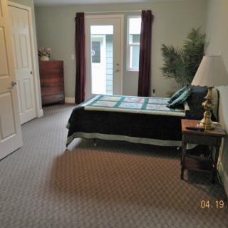 A cozy bedroom with a neatly made bed, side table, and a lamp by the window.