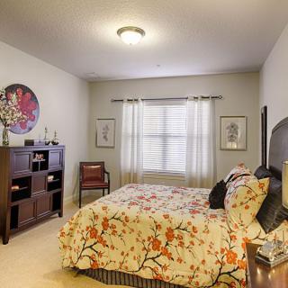 A cozy bedroom with floral bedding, a wooden bookshelf, and natural light from the window.
