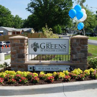 A welcoming entrance sign for 'The Greens at Long Creek' surrounded by colorful flowers and blue balloons.