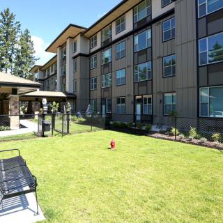A modern apartment building with a green lawn and outdoor seating area on a sunny day.
