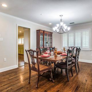 A stylish dining room with a wooden floor, elegant chandelier, and a well-set dining table.