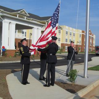 Uniformed personnel participate in a flag-raising ceremony outdoors, displaying the American flag.