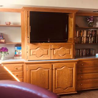 A wooden entertainment center with a television and shelves, designed for a cozy living room setting.
