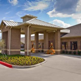A brick building with a covered entrance and well-maintained landscaping under a partly cloudy sky.