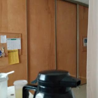 A coffee pot sits in the foreground with wooden cabinets and notes in the background.