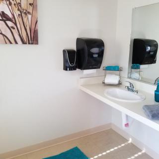 A clean and modern bathroom with a sink, mirror, and wall-mounted soap dispenser.