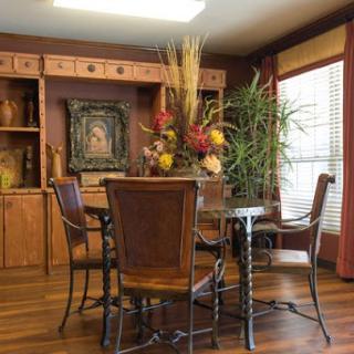 A cozy dining room featuring a wooden table surrounded by chairs, adorned with decorative plants and artwork.