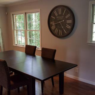 A dining room with a wooden table, chairs, and a large wall clock.