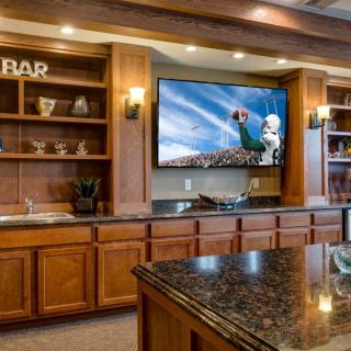 A cozy bar area with wooden cabinets and a large TV displaying a sports game.