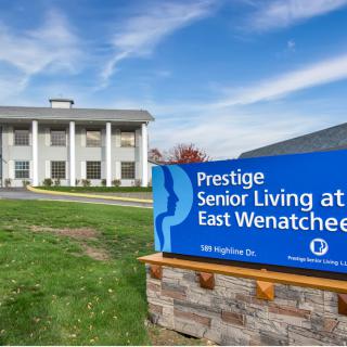The exterior view of Prestige Senior Living at East Wenatchee featuring a prominent sign and classic architectural style.