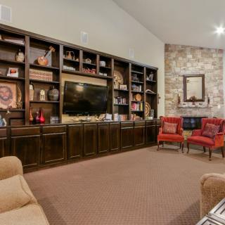A cozy living room with a large bookshelf, television, and comfortable seating area featuring two red chairs and a stone fireplace.