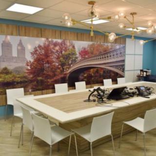 A modern conference room featuring a large mural of a bridge surrounded by autumn foliage, with sleek white chairs and contemporary lighting.