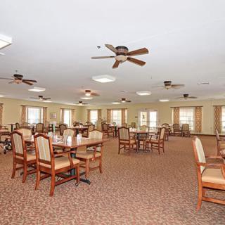 A spacious dining area with wooden tables and chairs, ceiling fans, and multiple windows.