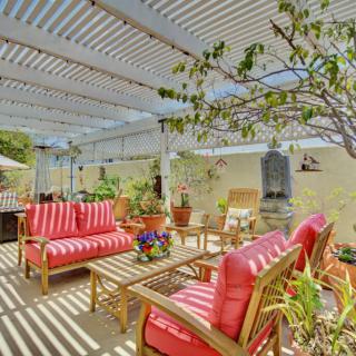 A cozy outdoor patio with colorful seating under a pergola, surrounded by lush greenery.