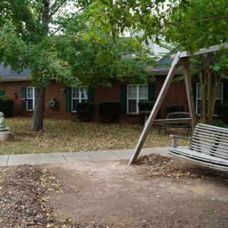 A peaceful yard with a swing and a house surrounded by trees and fallen autumn leaves.