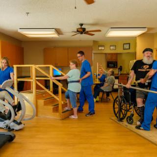 A rehabilitation session in a healthcare facility where patients receive assistance and therapy from medical staff.
