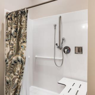A bathroom with an accessible shower featuring a floral curtain and a built-in shower seat.
