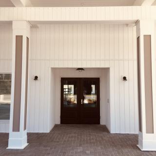 A modern building entrance with a white exterior and columns flanking a dark wooden door.