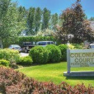A landscaped area with a sign reading 'Colonial Court', surrounded by trees and parked cars.